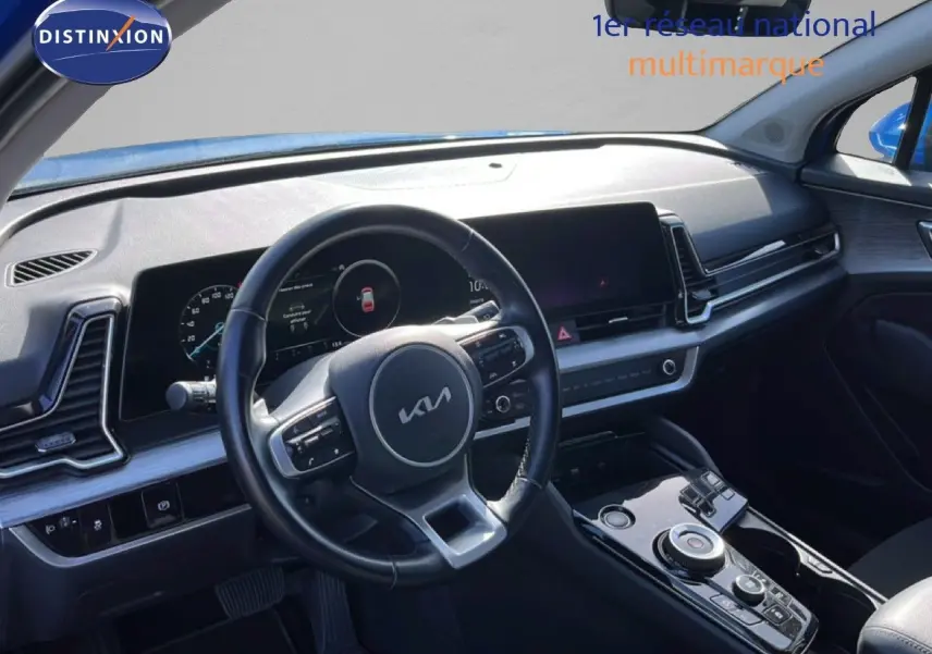 Vue intérieure du poste de conduite du Kia Sportage bleu fusion métal 2022, volant cuir multifonction et tableau de bord digital.