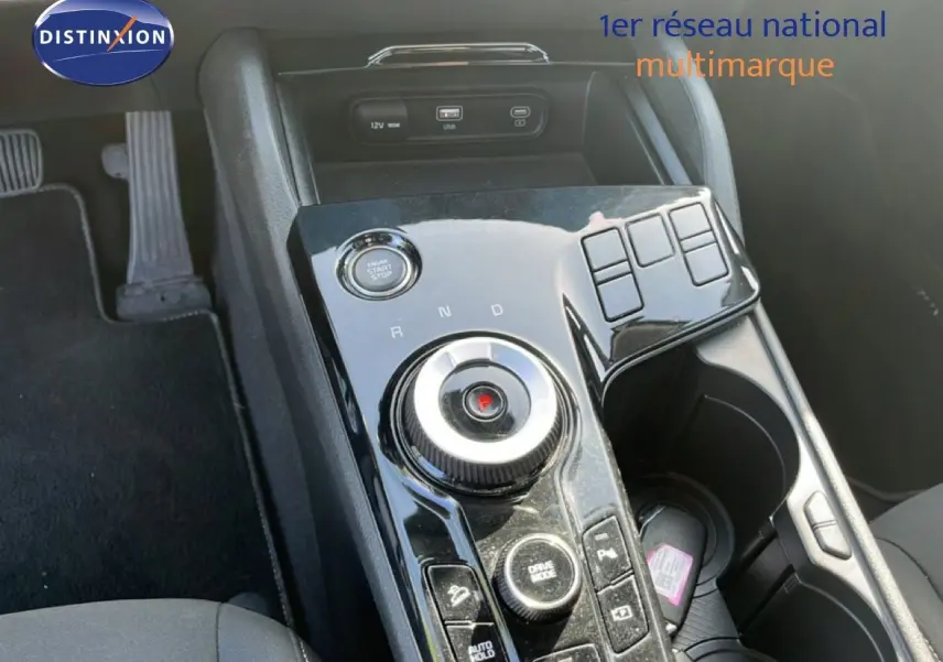 Vue rapprochée de la console centrale noire brillante du Kia Sportage 2022, avec molette de boîte auto et bouton start/stop.