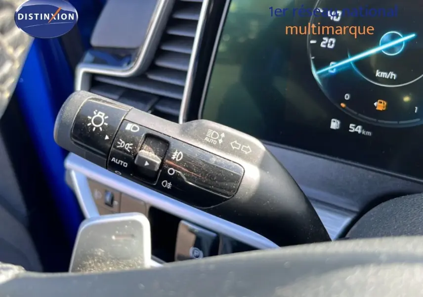 Gros plan sur la manette de clignotants et phares du KIA Sportage bleu fusion, avec tableau de bord numérique en arrière-plan.