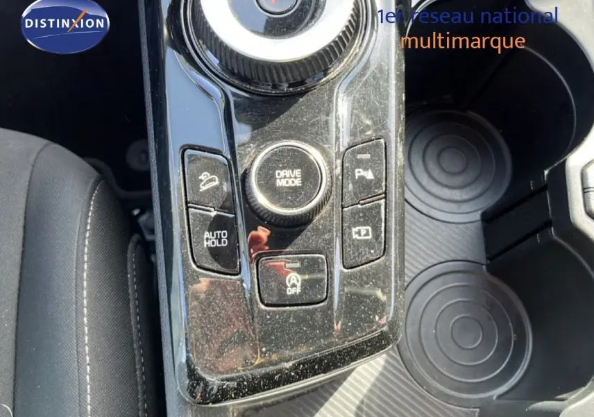 Vue rapprochée de la console centrale noire brillante du Kia Sportage bleu fusion, montrant les commandes de conduite et porte-gobelets.