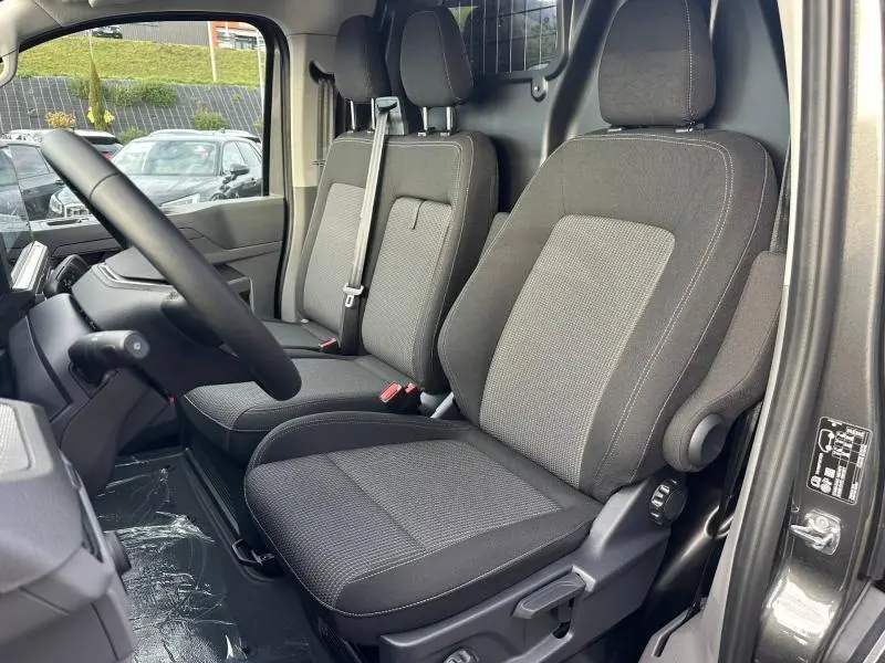 Vue intérieure côté conducteur du Volkswagen Transporter Procab gris 2025, montrant les sièges avant en tissu et la cloison métallique derrière.