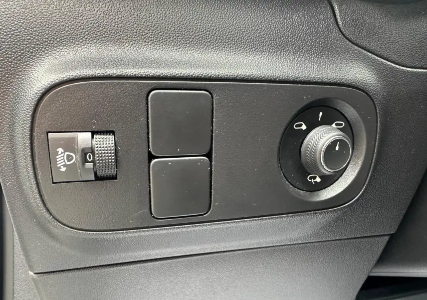 Gros plan sur les commandes noires de réglage des rétroviseurs et des phares d’un Citroën C3 blanc Banquise 2023.