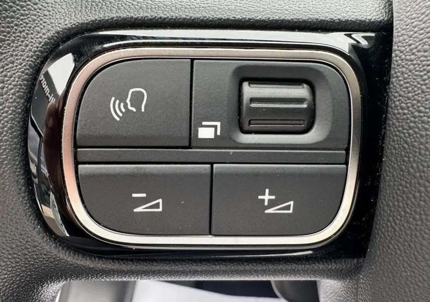 Gros plan sur les commandes du volant noir de la Citroën C3 blanche Banquise, boutons de réglage audio et vocal.
