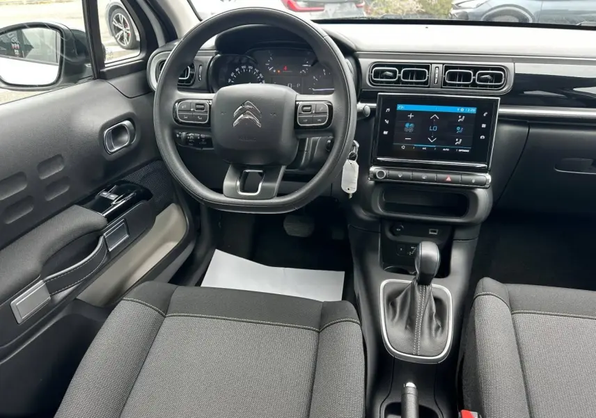 Vue intérieure avant de la Citroën C3 blanche, montrant le volant, l'écran tactile et la console centrale avec levier de vitesse automatique.