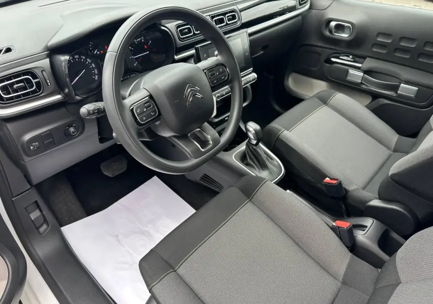 Vue intérieure côté conducteur de la Citroën C3 2023, montrant le volant, la console centrale avec écran tactile et sièges gris tissu Mica Grey.