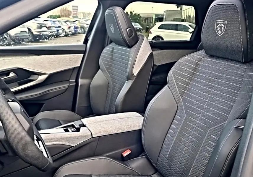 Vue intérieure côté conducteur du Peugeot 5008 Hybrid 145 GT avec sièges en tissu gris et cuir noir, logo Peugeot brodé.