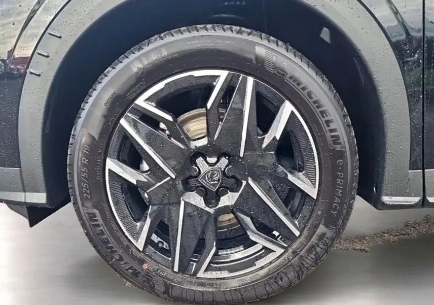 Gros plan sur la roue avant gauche noire du Peugeot 5008 Hybrid 145 GT e-dcs6 avec jante alu bicolore.