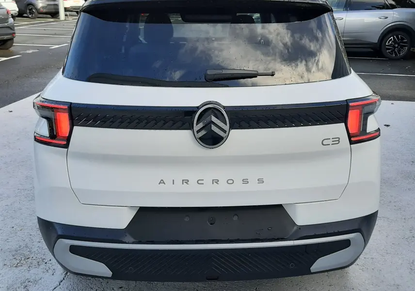 Vue arrière d'un Citroën C3 Aircross blanc avec toit noir, feux arrière allumés et logo central distinctif.