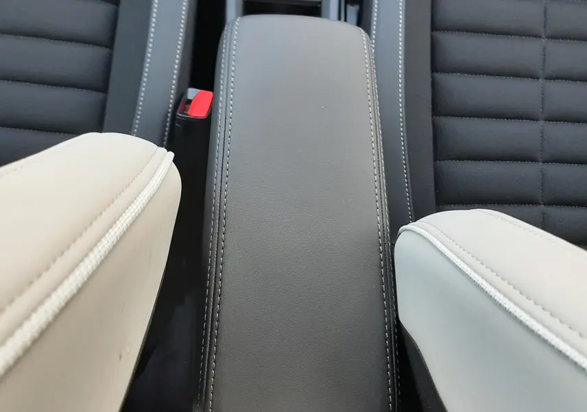 Vue rapprochée de l'accoudoir central noir avec surpiqûres blanches entre deux sièges tissu noir et cuir clair du Citroën C3 Aircross hybride.