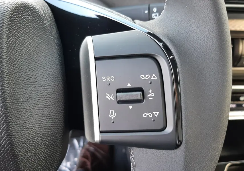 Gros plan sur les commandes multifonctions noires à gauche du volant gris du Citroën C3 Aircross hybride 2026.