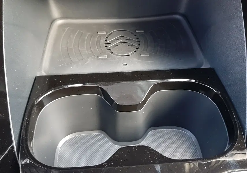Gros plan intérieur sur le compartiment porte-gobelets noir brillant avec zone de charge sans fil et logo Citroën embossé.