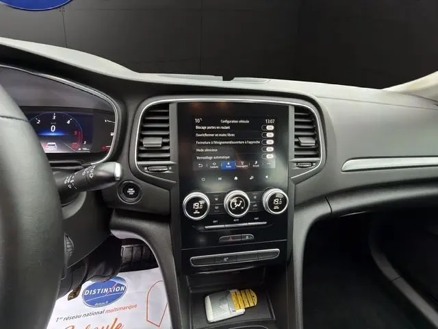 Vue intérieure centrée sur la console centrale tactile de la Renault Mégane IV blanche, avec commandes climatisation et tableau de bord partiel.