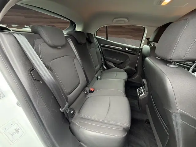 Vue intérieure arrière côté gauche de la Renault Mégane IV blanche, sièges tissu noir avec ceintures de sécurité visibles.