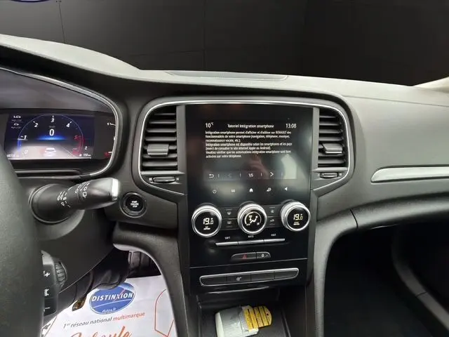 Vue intérieure du tableau de bord de la Renault Mégane IV blanche, avec écran tactile central et commandes de climatisation.