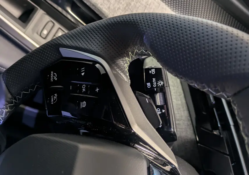 Gros plan sur le volant perforé et les commandes intégrées côté gauche du Peugeot 3008 gris titanium, avec détail du tissu de porte.