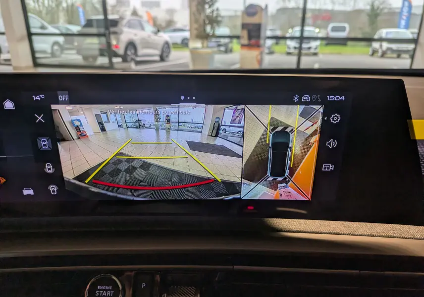 Écran de caméra 360° du Peugeot 3008 gris titanium montrant une vue arrière et une vue aérienne du stationnement intérieur.