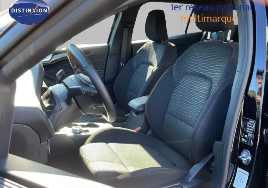 Vue intérieure côté conducteur de la Ford Focus SW noire, sièges tissu avec surpiqûres rouges et volant cuir multifonction.