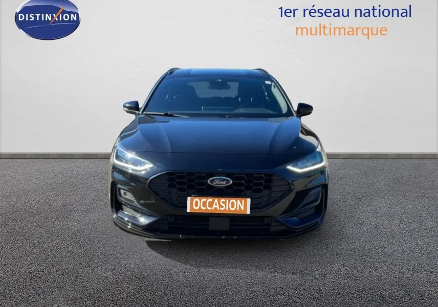 Vue frontale d'une Ford Focus SW noire Agate Metal 2024 avec calandre hexagonale et phares LED allumés.