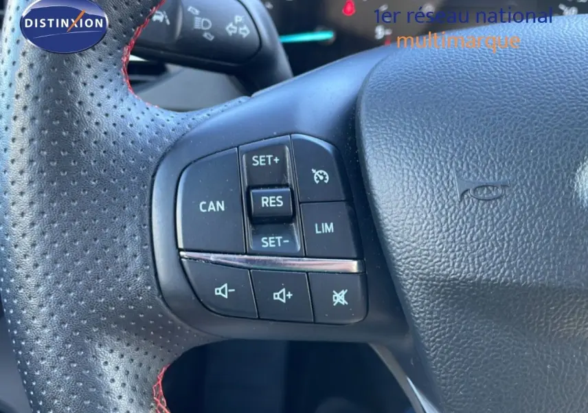 Gros plan sur le volant noir perforé avec surpiqûres rouges de la Ford Focus SW 2024, boutons de régulateur de vitesse visibles.
