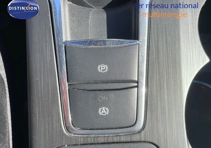 Gros plan sur la console centrale de la Ford Focus SW noire, mettant en valeur les boutons du frein à main électrique et de l'assistance au démarrage.