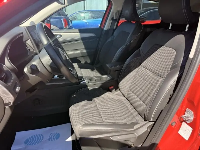 Vue intérieure côté conducteur du Renault Arkana rouge flamme 2022, sièges en tissu noir et console centrale visible.