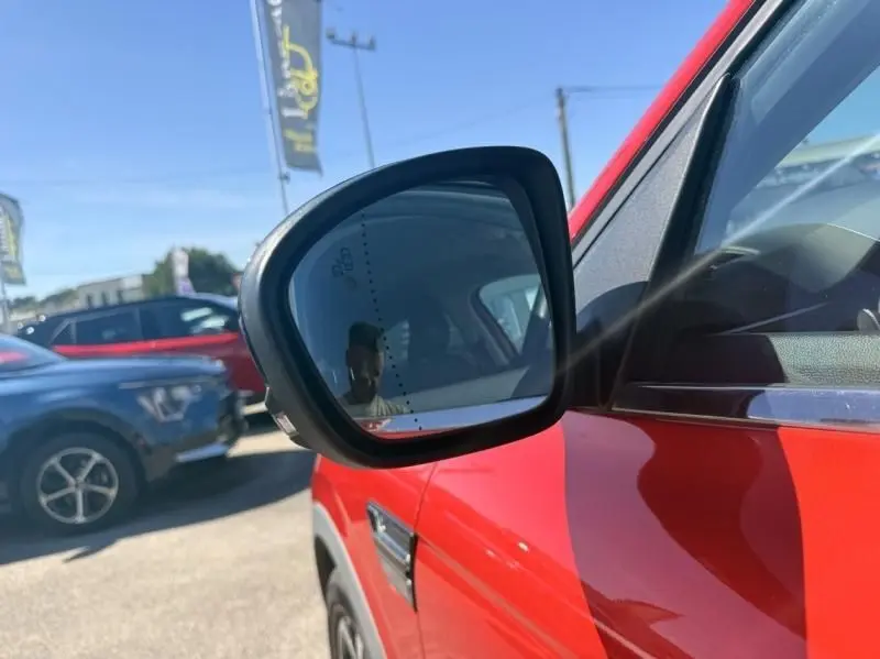 Rétroviseur côté gauche d’un Renault Arkana rouge flamme 2022, avec reflet et partie de la portière visible.