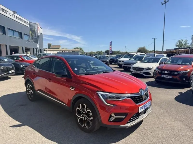 Renault Arkana 1.6 E-Tech rouge flamme en 3/4 avant droit, avec jantes distinctives et calandre marquée.