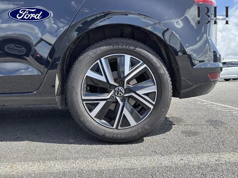 Gros plan sur la roue arrière droite d’un Volkswagen Touran noir intense nacré avec jante alu bicolore et logo VW central.