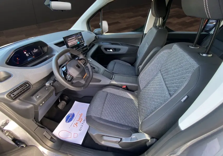 Vue intérieure côté conducteur du Peugeot Rifter 2025 gris acier, avec tableau de bord numérique et sièges tissu gris.