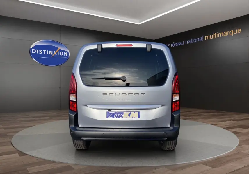Vue arrière du Peugeot Rifter gris acier 2025 avec hayon vitré et feux arrière verticaux allumés.