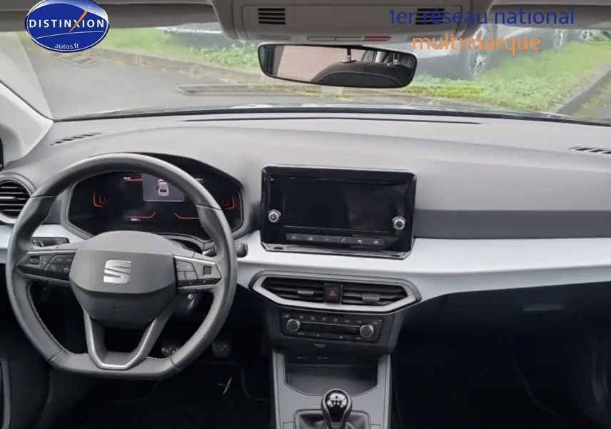 Vue intérieure avant du tableau de bord gris clair et noir de la SEAT Ibiza 2025 avec volant multifonction et boîte manuelle.