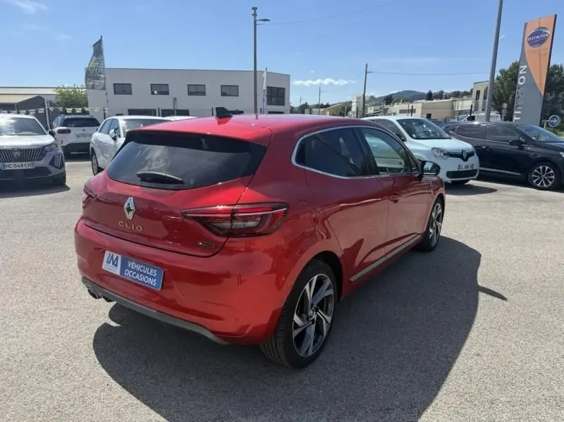 Renault Clio V 1.0 TCE 90 RS Line rouge flamme vue 3/4 arrière droit sur parking ensoleillé.