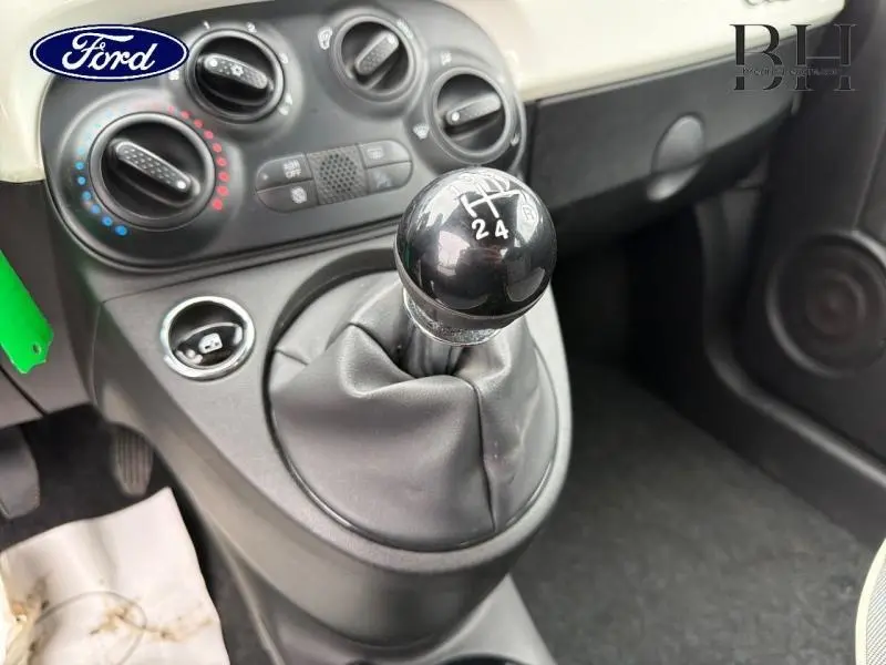 Gros plan sur le levier de vitesses manuel noir et la console centrale grise d'une Fiat 500 blanche, intérieur épuré.