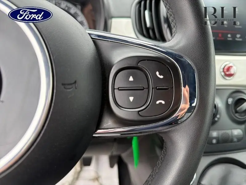 Gros plan sur les commandes au volant cuir noir de la FIAT 500 blanche, avec boutons de gestion d'appels et navigation.