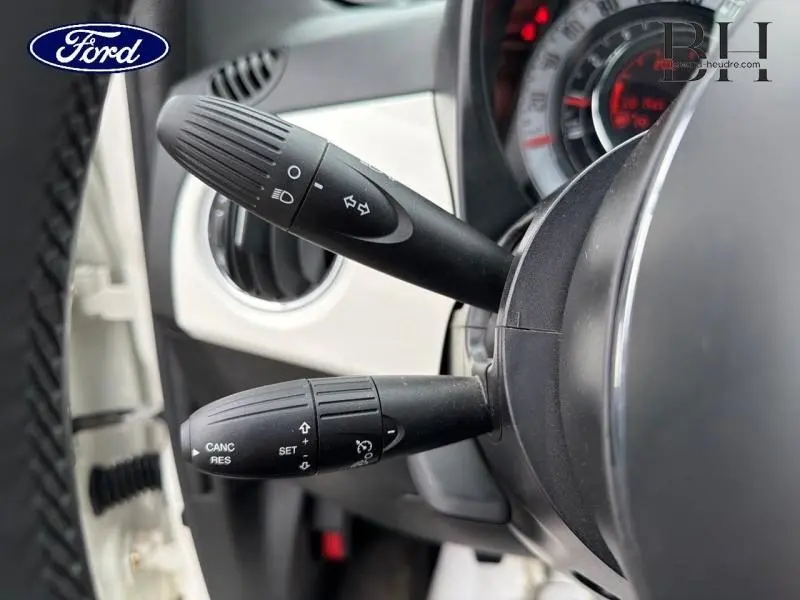 Gros plan sur les commandes de clignotants et régulateur de vitesse à gauche du volant d’une Fiat 500 blanche.