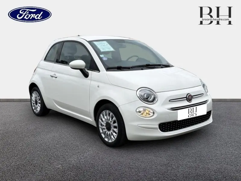 Vue 3/4 avant d'une FIAT 500 blanche Bossa Nova Pastel avec jantes alu et phares allumés.