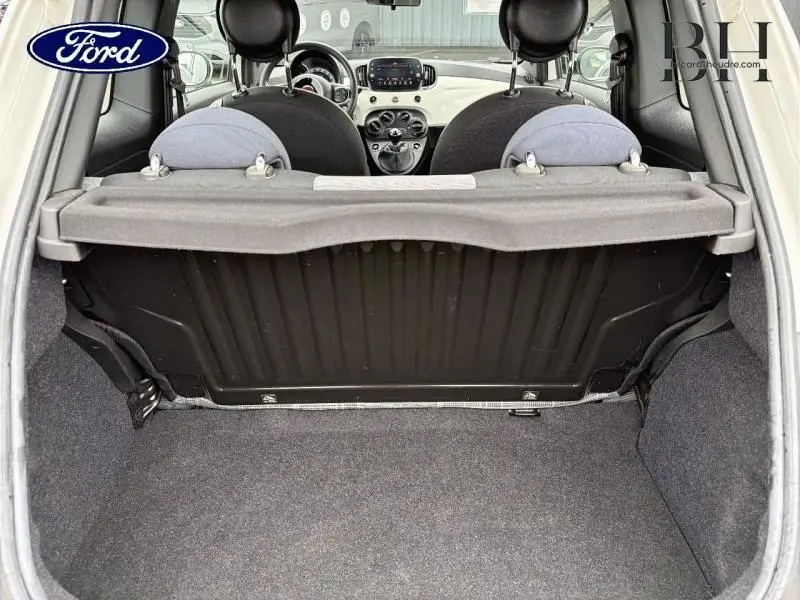 Vue depuis le coffre ouvert d'une Fiat 500 blanche, montrant l'intérieur avec sièges arrière et tableau de bord.
