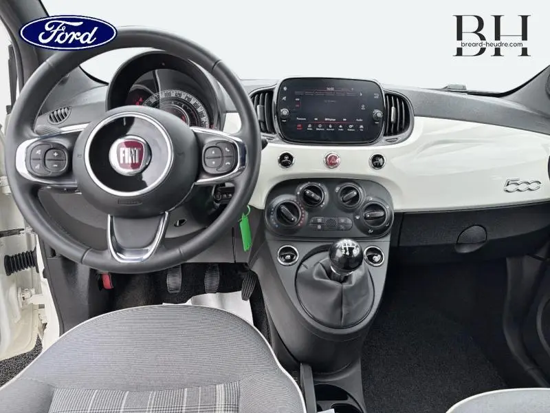 Intérieur avant de la Fiat 500 blanche, vue centrée sur le volant cuir, tableau de bord brillant et levier de vitesse manuel.