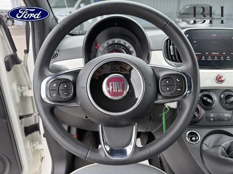 Vue intérieure centrée sur le volant cuir noir de la Fiat 500 Bossa Nova White Pastel avec tableau de bord et écran tactile visibles.