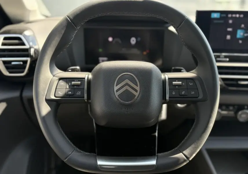 Gros plan sur les commandes gauche du volant noir de la Citroën C4 Hybrid 145 CH, avec tableau de bord flou en arrière-plan.