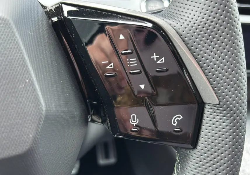 Gros plan sur les commandes noires brillantes du volant perforé du Peugeot 3008 Hybrid 2026.