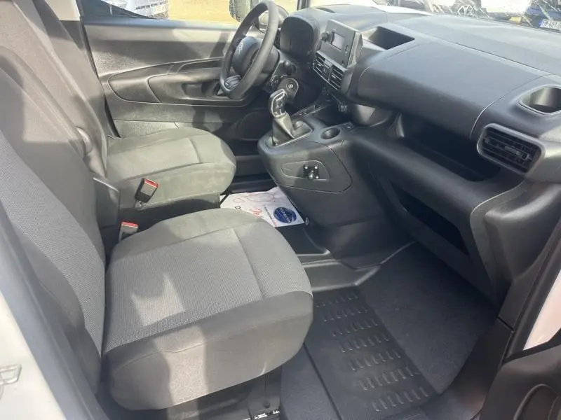 Intérieur avant du Citroën Berlingo Fourgon blanc, vue côté conducteur montrant sièges gris et tableau de bord noir.