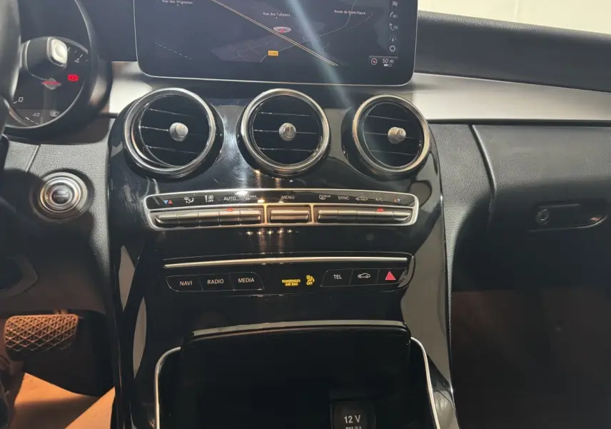 Vue rapprochée du tableau de bord noir brillant de la Mercedes Classe C Break C 200 d avec écran de navigation et commandes climatisation.