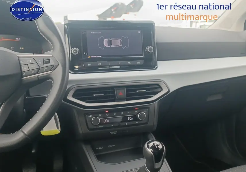 Vue intérieure centrée sur la console centrale et le volant cuir noir de la SEAT Ibiza blanc Nevada 2025 avec boîte manuelle.