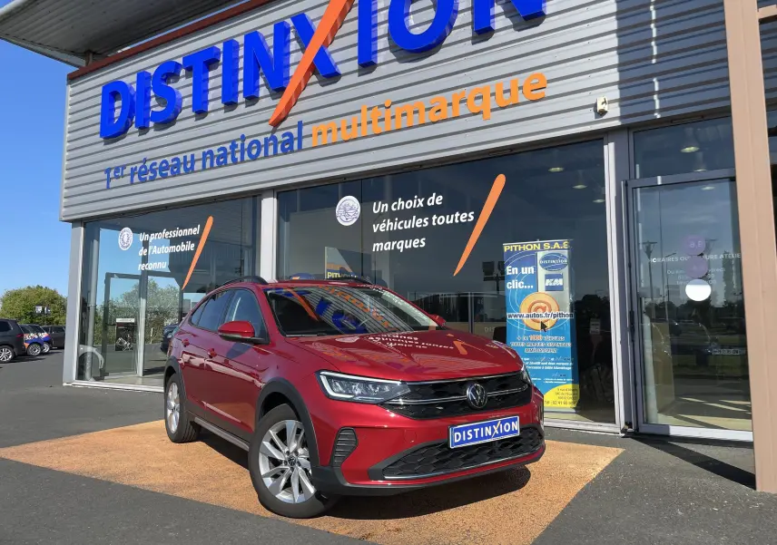 Volkswagen Taigo rouge roi en 3/4 avant droit devant un showroom Distinxion, avec jantes alliage et calandre noire.