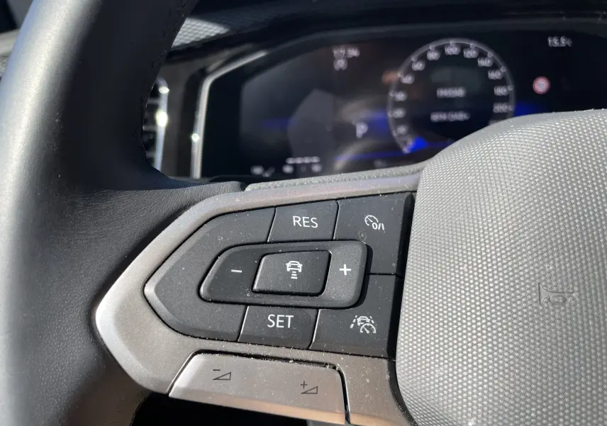 Gros plan sur les commandes au volant côté gauche du Volkswagen Taigo 2024, intérieur gris noir avec boutons de régulateur de vitesse.