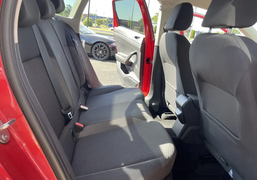 Vue intérieure arrière côté gauche du Volkswagen Taigo rouge roi 2024, montrant les sièges arrière en tissu gris foncé.