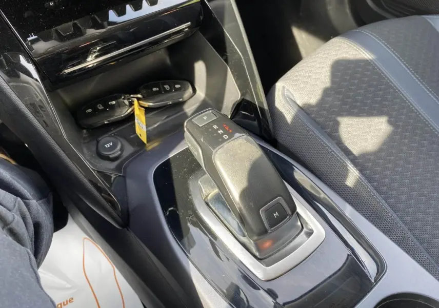 Gros plan sur la console centrale de la Peugeot 2008 2020, montrant le levier de boîte auto et les clés sur fond noir brillant.
