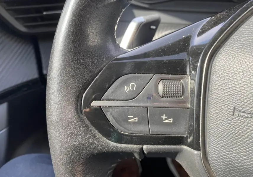 Gros plan sur les commandes de volume et téléphone au volant noir du Peugeot 2008 gris clair, version 2020.