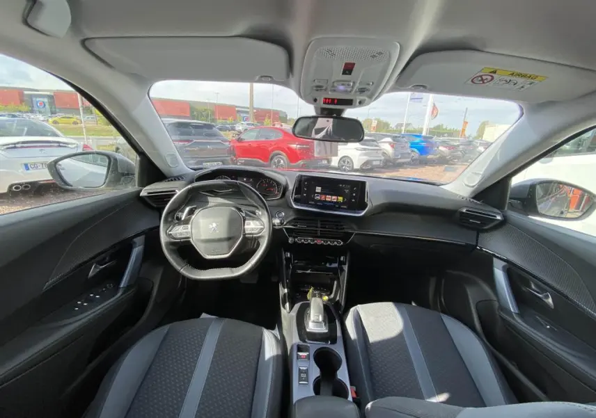 Vue intérieure avant de la Peugeot 2008 gris clair, montrant le tableau de bord, le volant et l’écran tactile central.